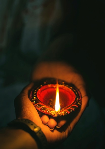 Hand holding another hand that is holding a small Diwali oil lamp.